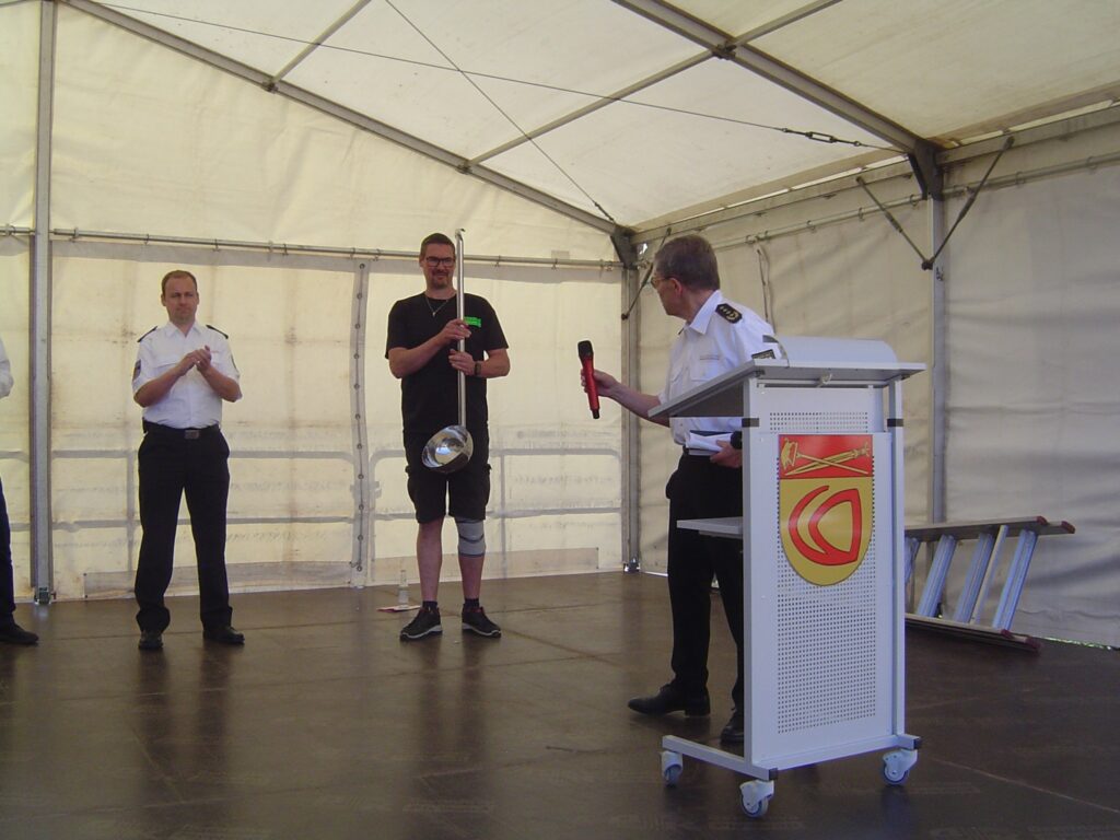 Ehrenlandesbrandinspekteur Bernd Becker (rechts) überreicht Dominik Thiry (Bildmitte) eine Schöpfkelle. Links im Bild: Gemeindewehrführer Alexander Kuhn. Foto: Manfred Koch, Pressebeauftragter Freiwillige Feuerwehr Gemeinde Nonnweiler